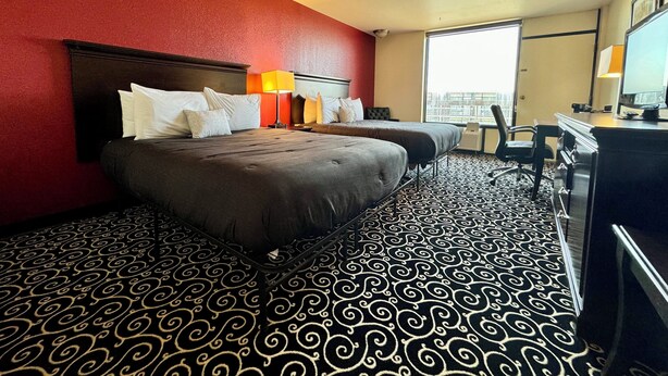 Una habitación de hotel con dos camas, un escritorio, una silla y un ventanal grande.