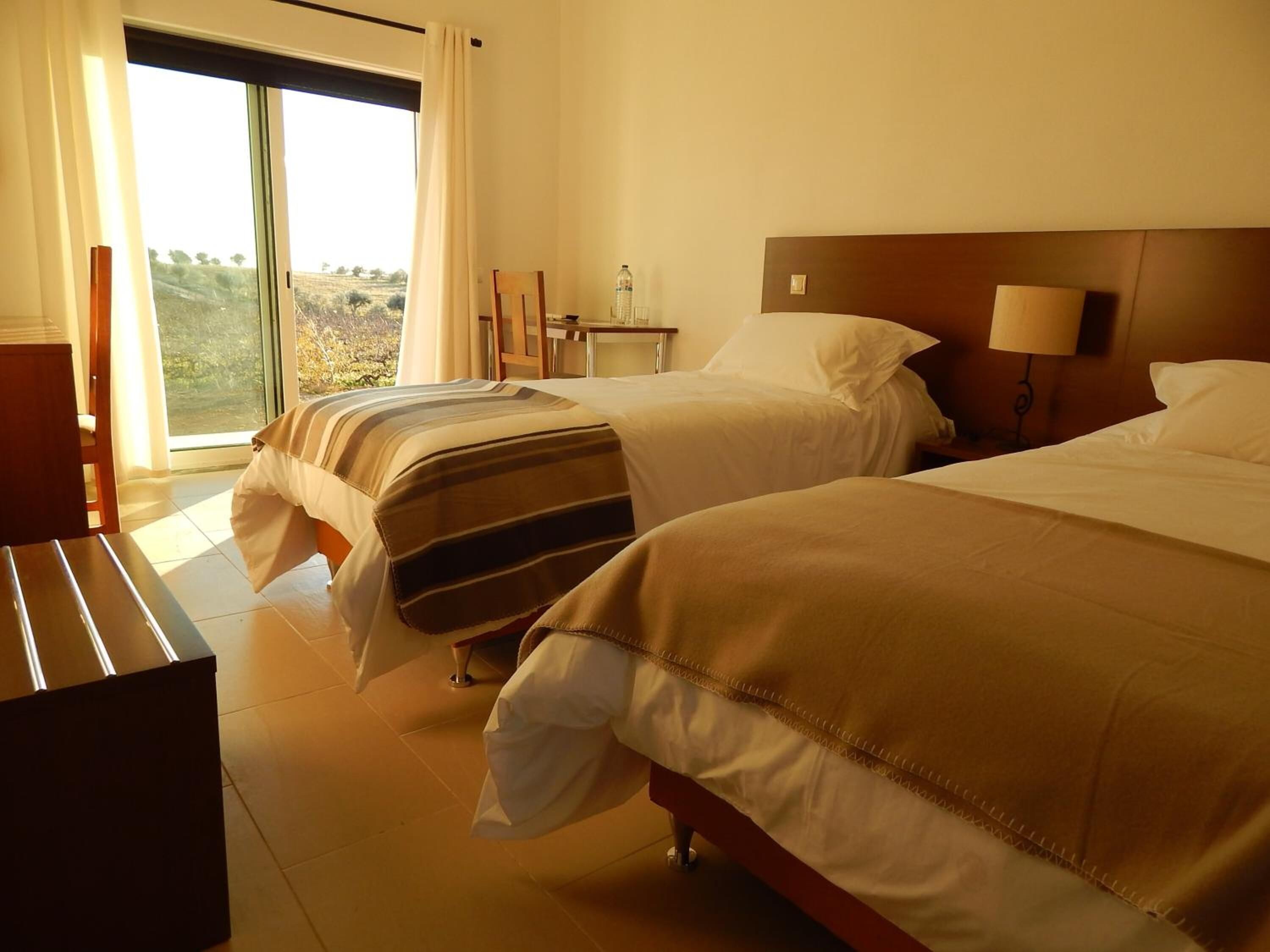 Habitación de hotel con dos camas, un escritorio, una silla y vistas al exterior.
