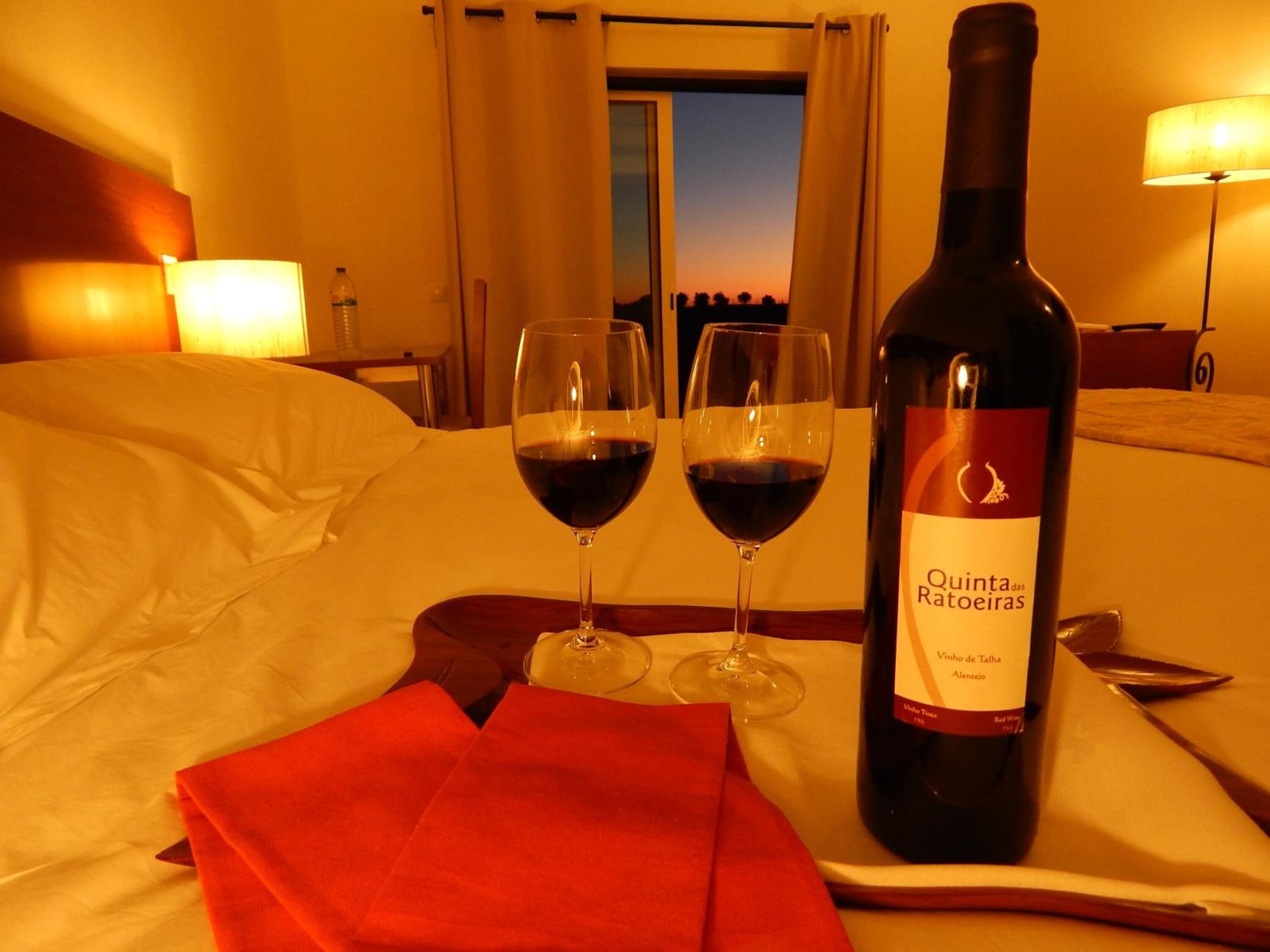 A hotel room with a bed, two wine glasses, and a bottle of Quinta das Ratoeiras wine on a tray.