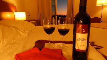 A hotel room with a bed, two wine glasses, and a bottle of Quinta das Ratoeiras wine on a tray.
