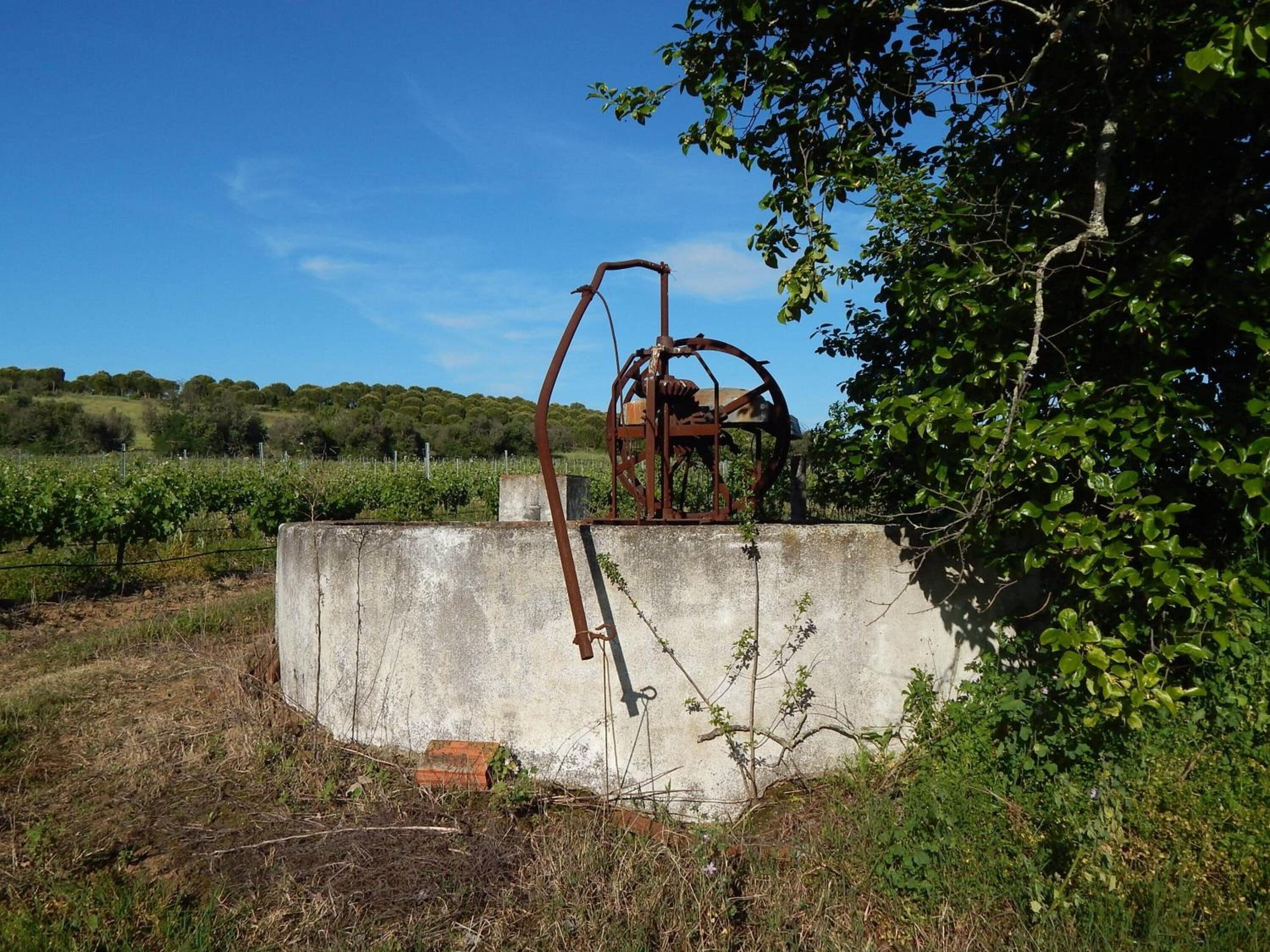 Eine alte, verrostete Metallkonstruktion in ländlicher Umgebung mit Betonfundament, umgeben von Grün und blauem Himmel.