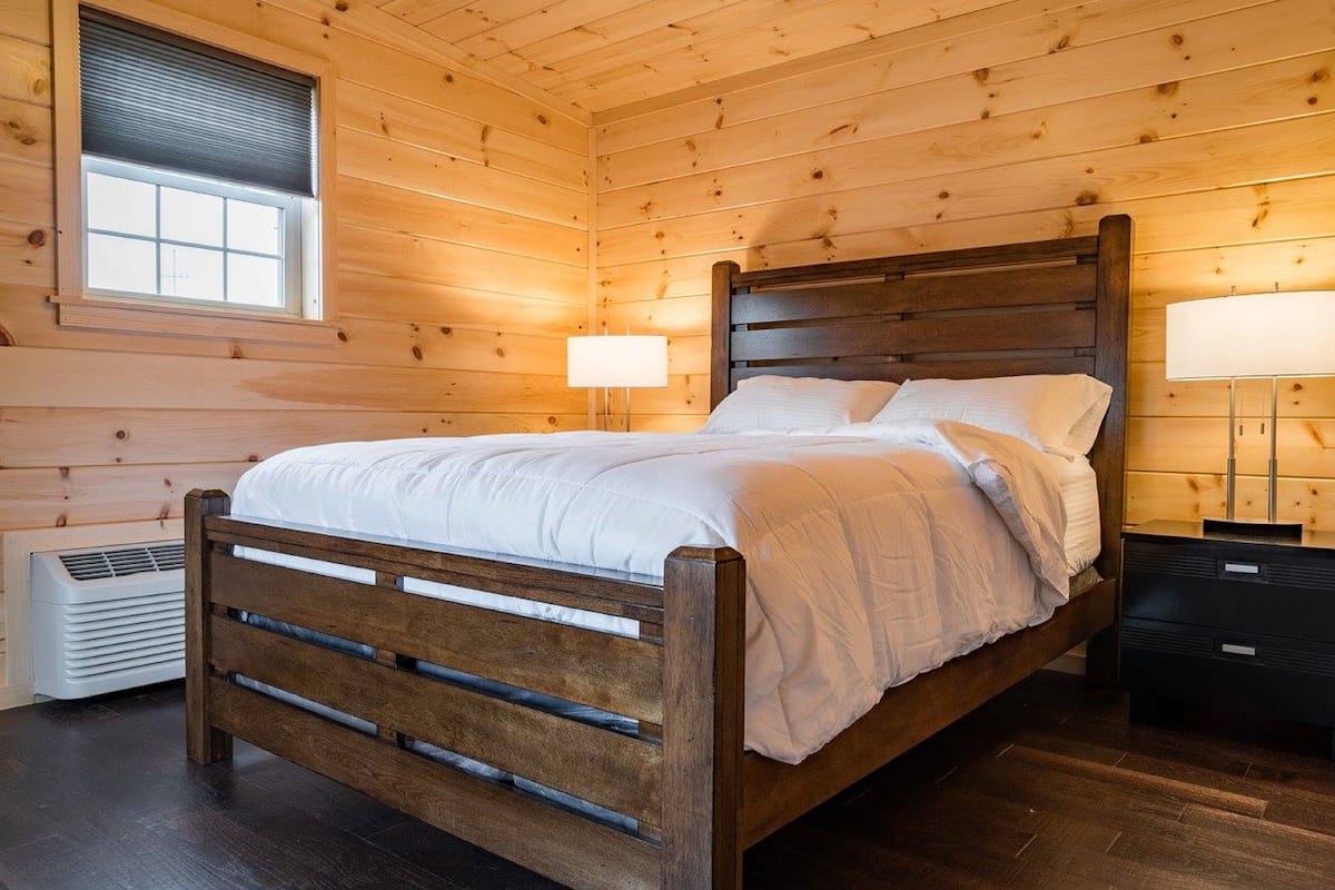 A wooden-paneled bedroom with a bed, bedside lamps, and a window.