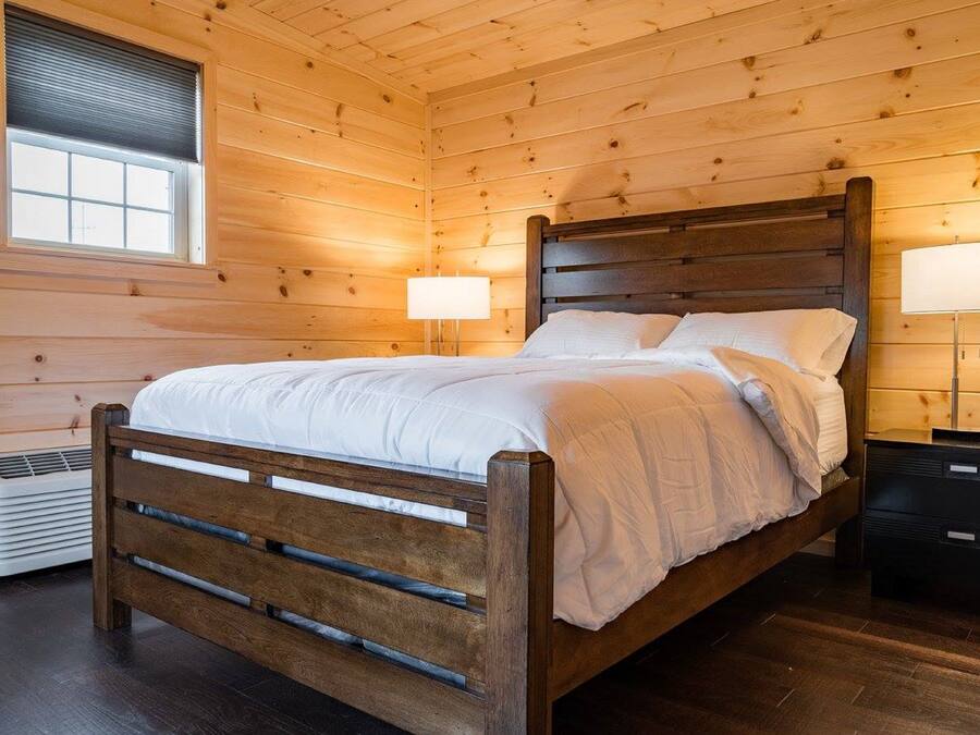 Un dormitorio con paneles de madera, una cama, lámparas de noche y una ventana.