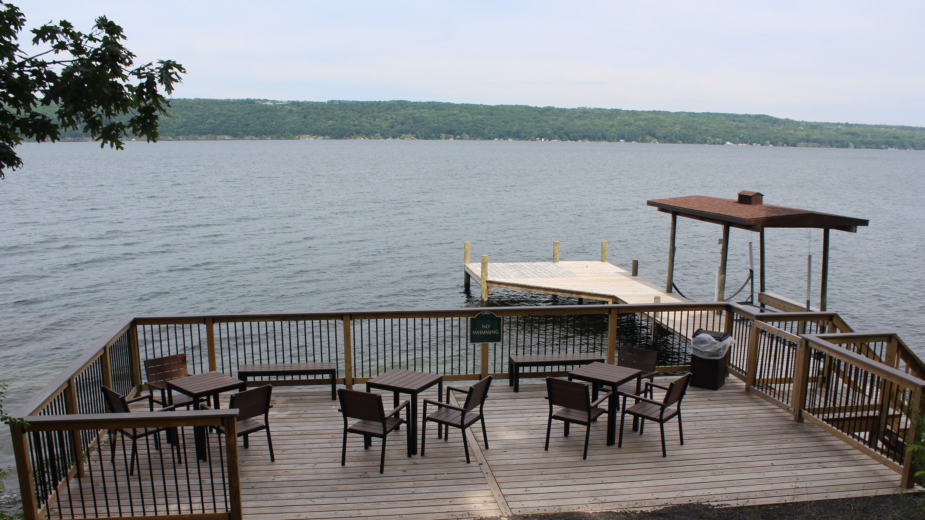 A wooden deck with tables and chairs overlooking a lake.
