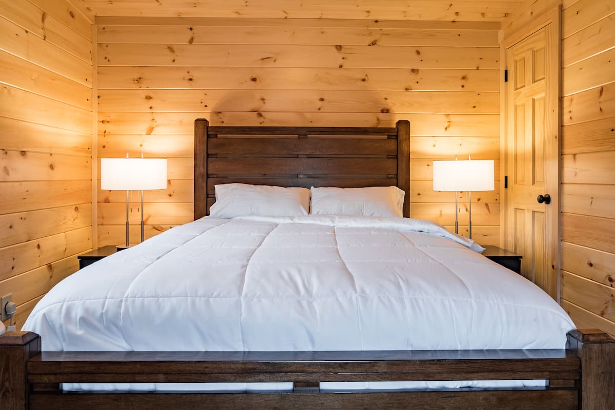 A wooden cabin bedroom with a large bed, two bedside lamps, and a wooden headboard.