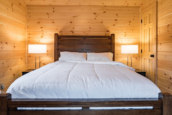 Un dormitorio de cabaña de madera con una cama grande, dos lámparas de noche y un cabecero de madera.