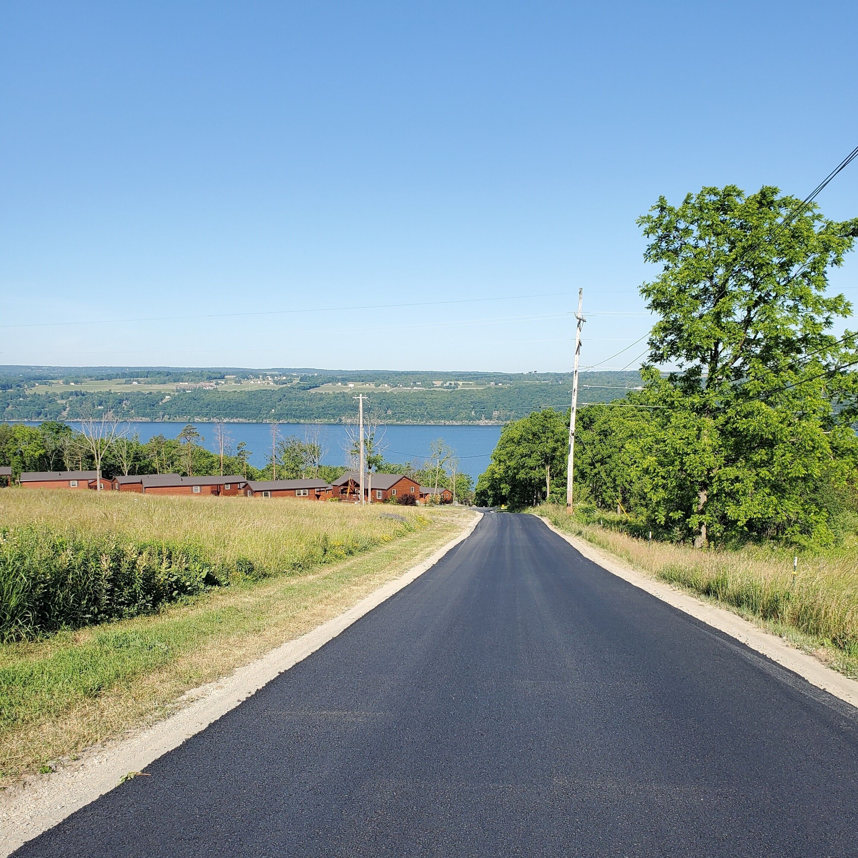 A rural road with houses on one side and a lake in the distance.