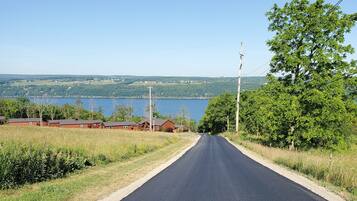 A rural road with houses on one side and a lake in the distance.