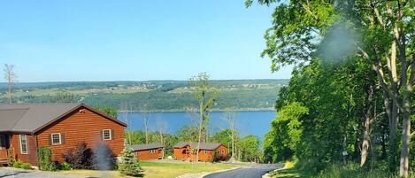 A rural road with a wooden cabin and a lake in the background.