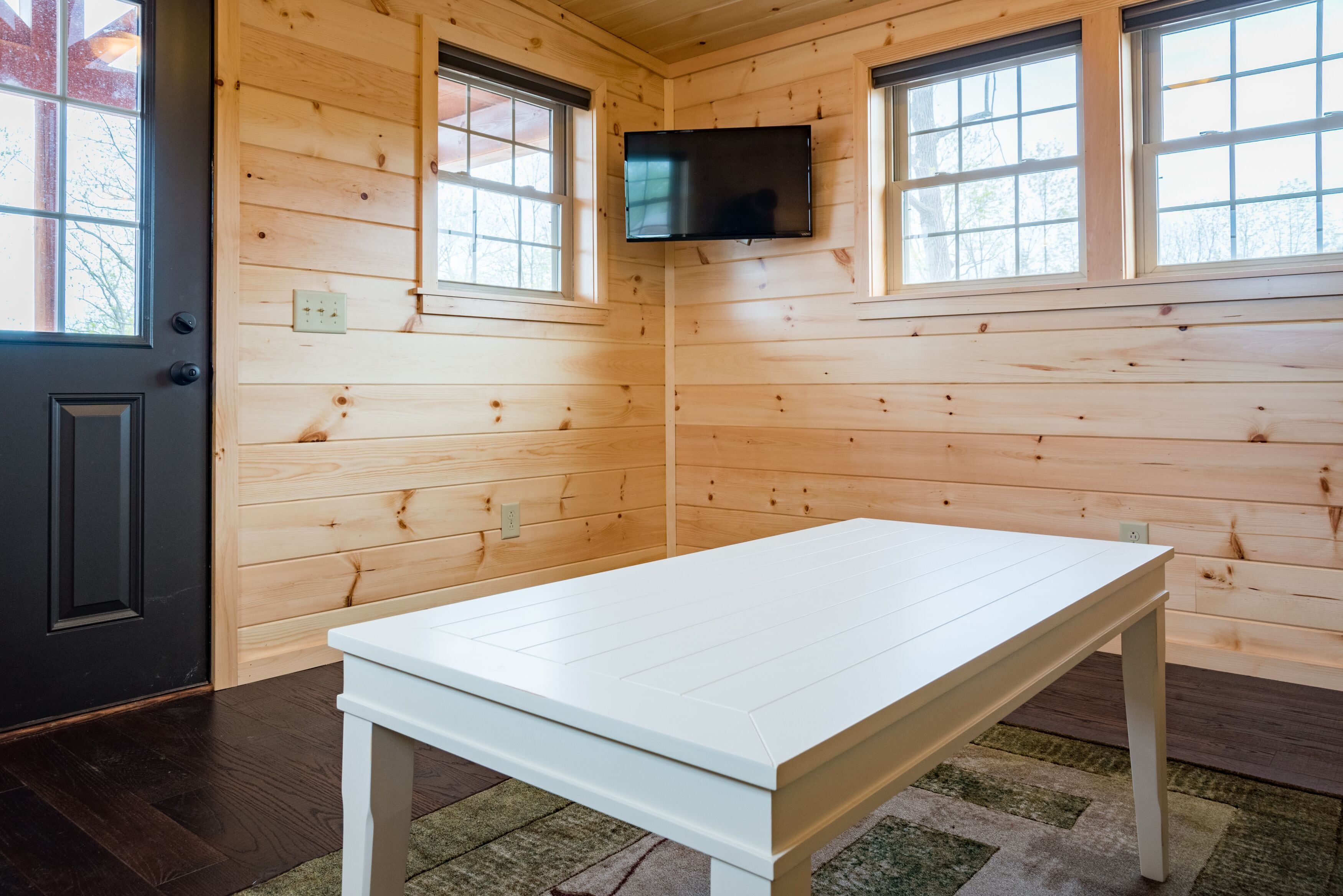A room with wooden walls, a white table, and a TV mounted on the wall.