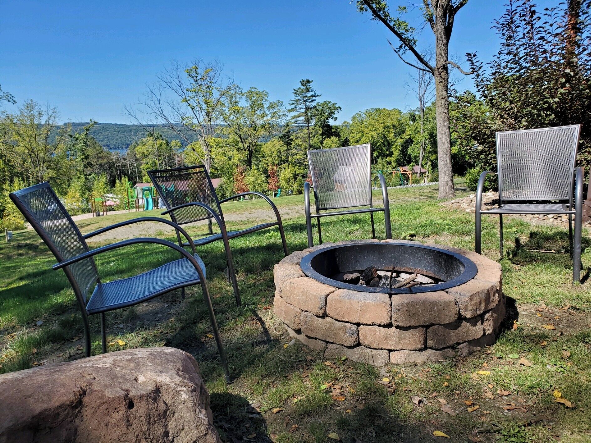 A fire pit with metal chairs and a stone fire ring in a grassy outdoor area.