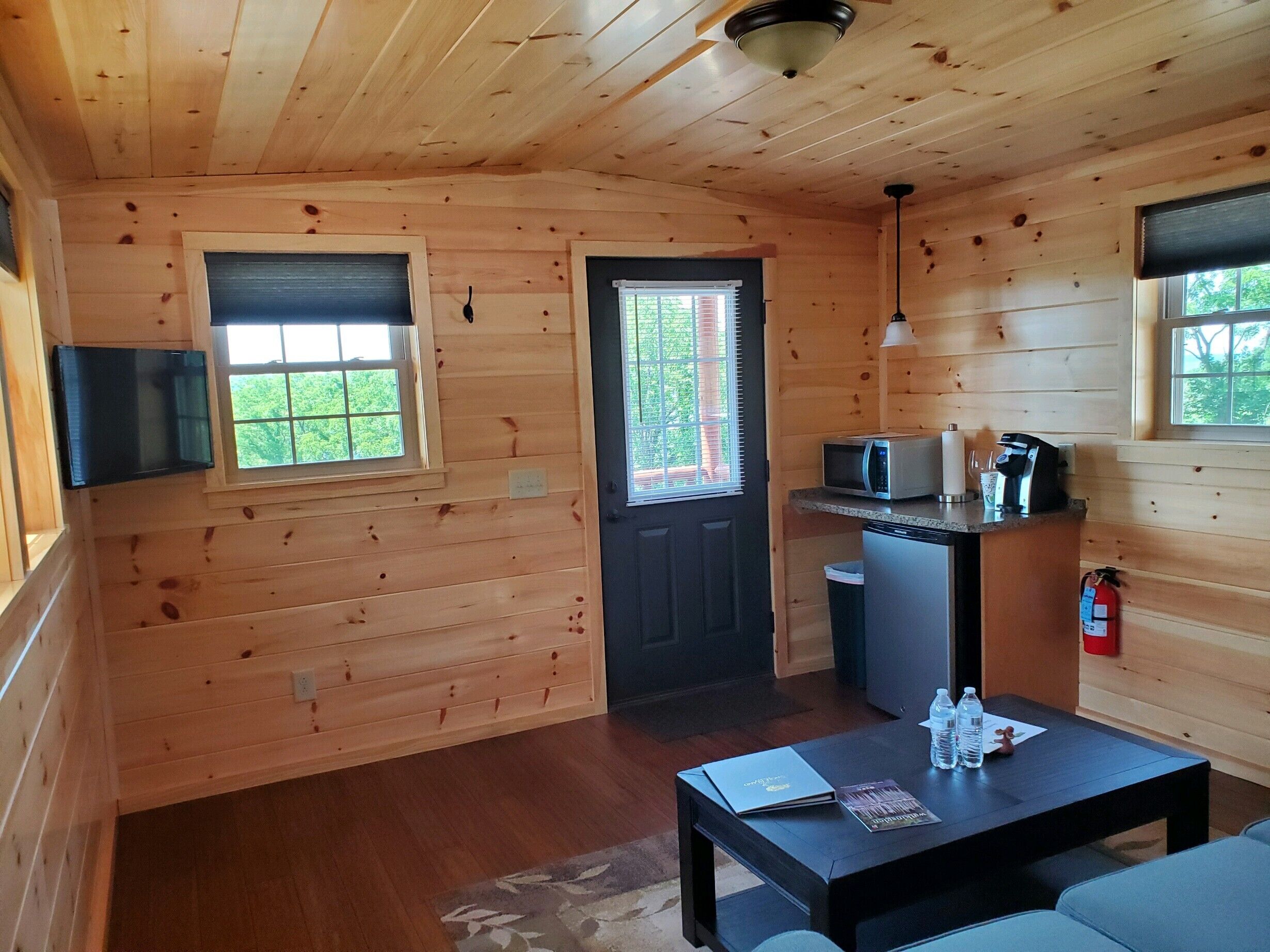 A compact wooden cabin with a kitchenette, a dining table with chairs, and a small window with blinds.