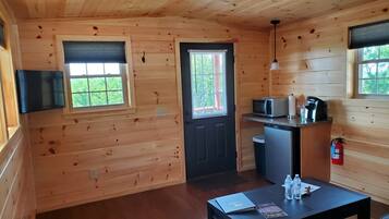 A compact wooden cabin with a kitchenette, a dining table with chairs, and a small window with blinds.