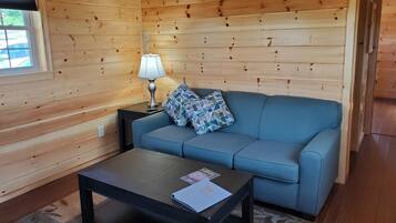 A cozy room with wooden walls, a blue sofa, a small table with a lamp, and a window.