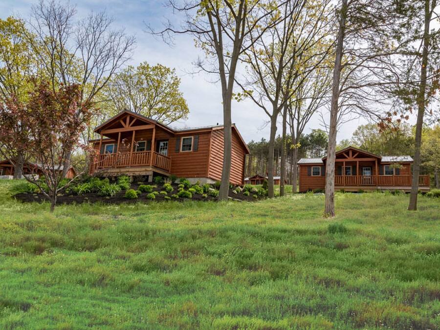A wooden cabin with a balcony, surrounded by trees and grassy area.