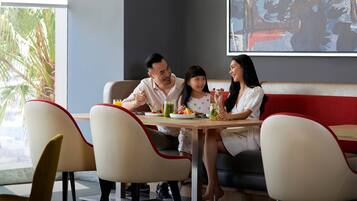 A family dining at a restaurant with a modern interior, including a large screen displaying a scene, a casual seating arrangement, and a view of palm trees outside.