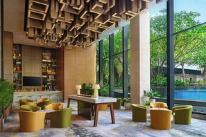 A modern lobby with a bar area, seating, and large windows overlooking a pool. - Four Points by Sheraton Surabaya, Tunjungan Plaza (Surabaya)