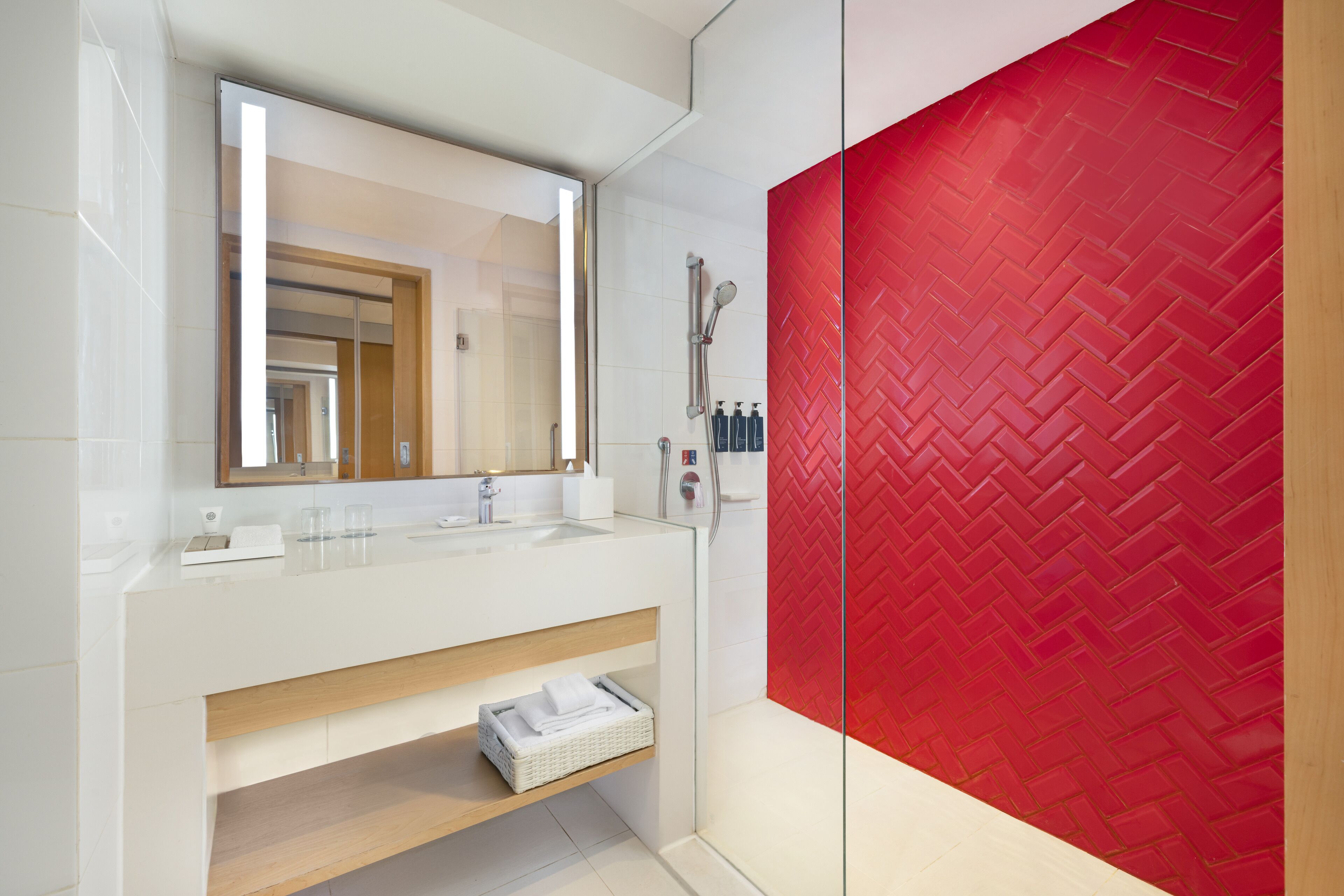 A modern bathroom with a white vanity, a large mirror, a red herring-patterned wall, and a shower area.