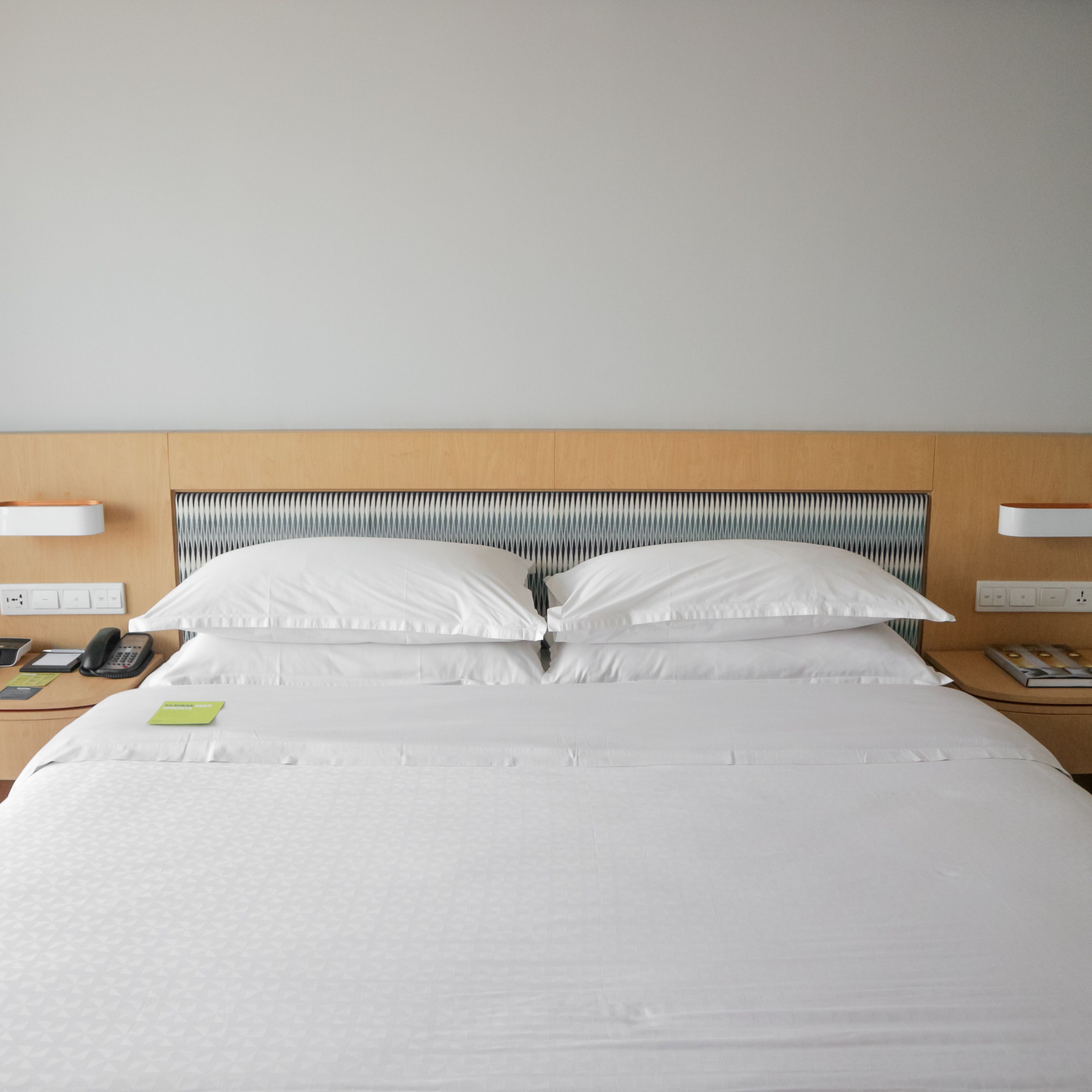 A neatly made bed with white linens, a wooden headboard, bedside tables with lamps, and a phone on the left side.