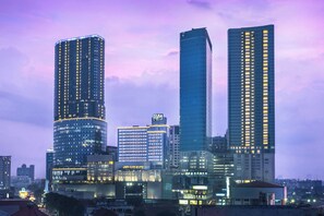 A cityscape with modern high-rise buildings, including a prominent curved skyscraper and a tall rectangular building with illuminated windows. - Four Points by Sheraton Surabaya, Tunjungan Plaza (Surabaya)