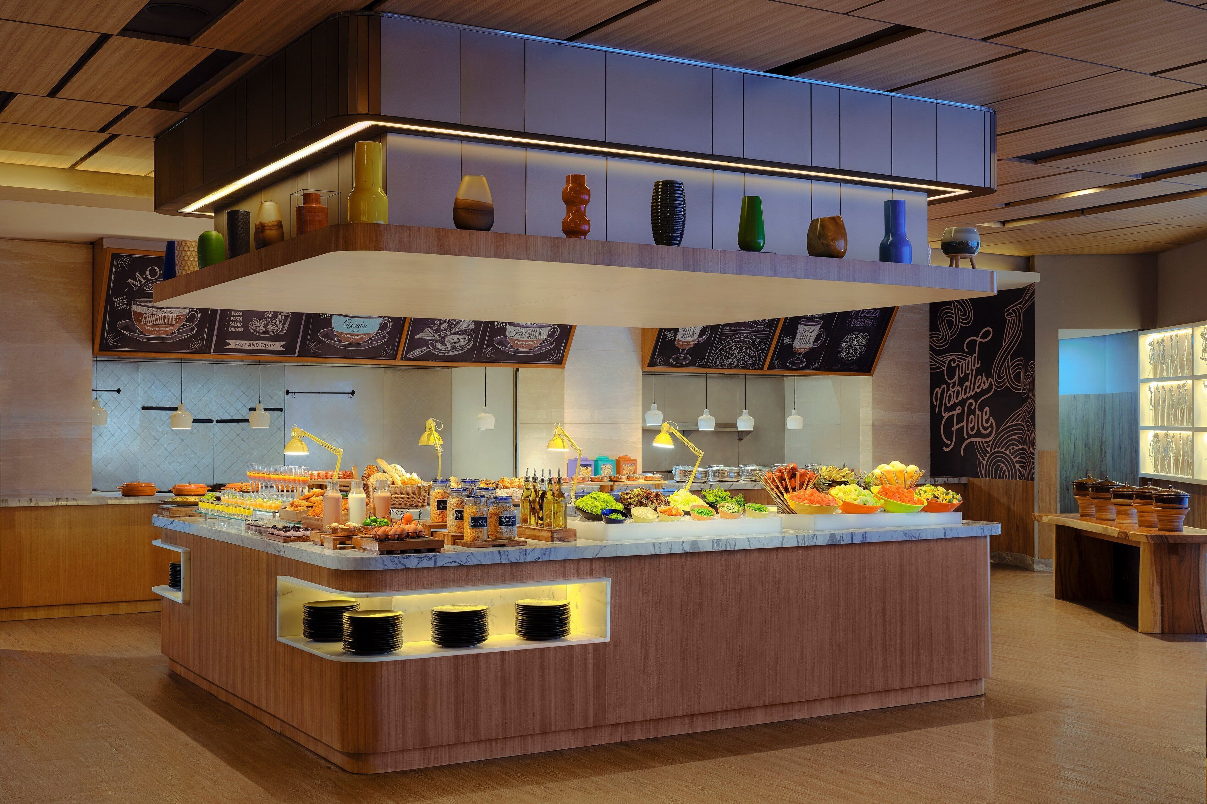 A buffet area with a variety of food items and beverages, wooden paneling, and pendant lighting.