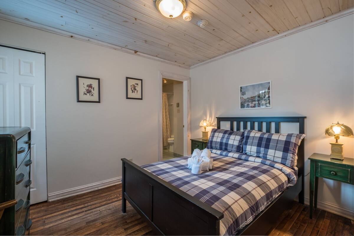 A bedroom with a bed, two bedside tables with lamps, a door, and two framed pictures on the wall.