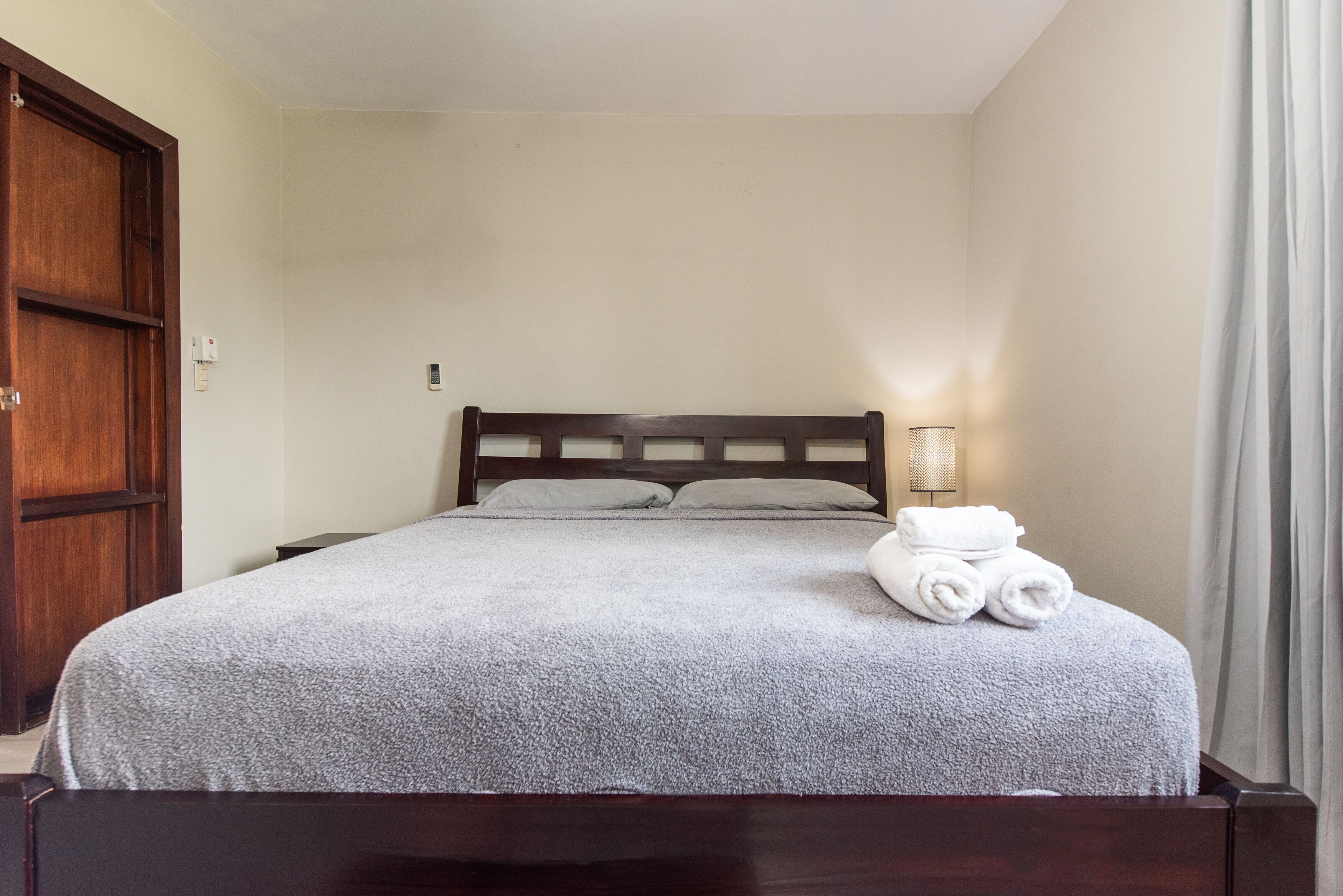 A neatly made bed with a grey blanket, a wooden headboard, and a bedside lamp.