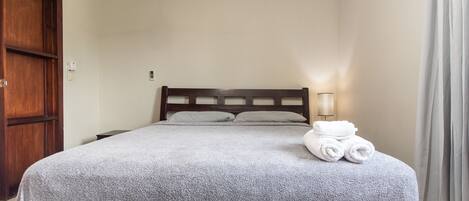 Una cama bien hecha con una manta gris, un cabecero de madera y una lámpara de noche.