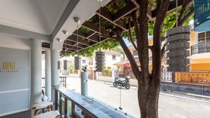 A covered outdoor seating area with a view of the street, a tree, and a building with a sign that reads "RESTAURANT". - Hotel Casa Jum (Santiago de los Caballeros)