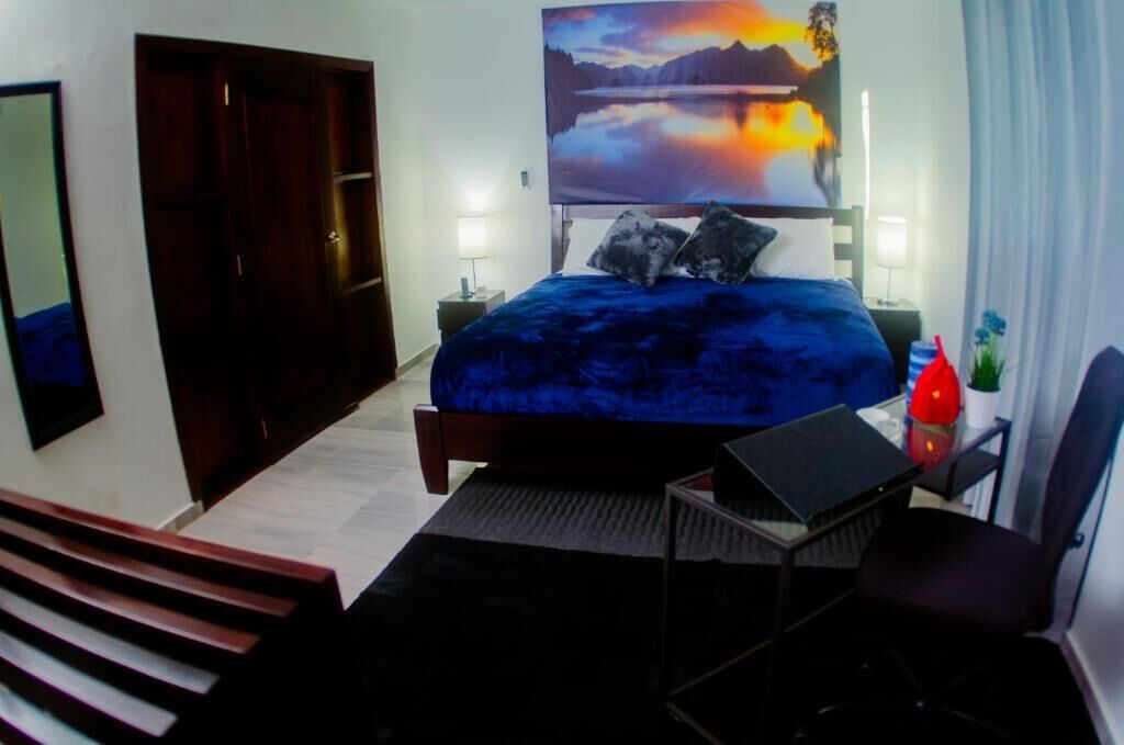 Un dormitorio con una cama grande, un escritorio, una silla, una mesita de noche y un cuadro en la pared.