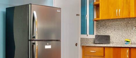 A compact kitchen with a stainless steel refrigerator, wooden cabinets, and a granite countertop.