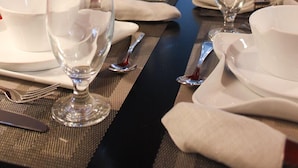 A dining table set for four with clear glassware and white plates, positioned in a room with a view of a garden through a glass door. - Hotel Casa Jum (Santiago de los Caballeros)