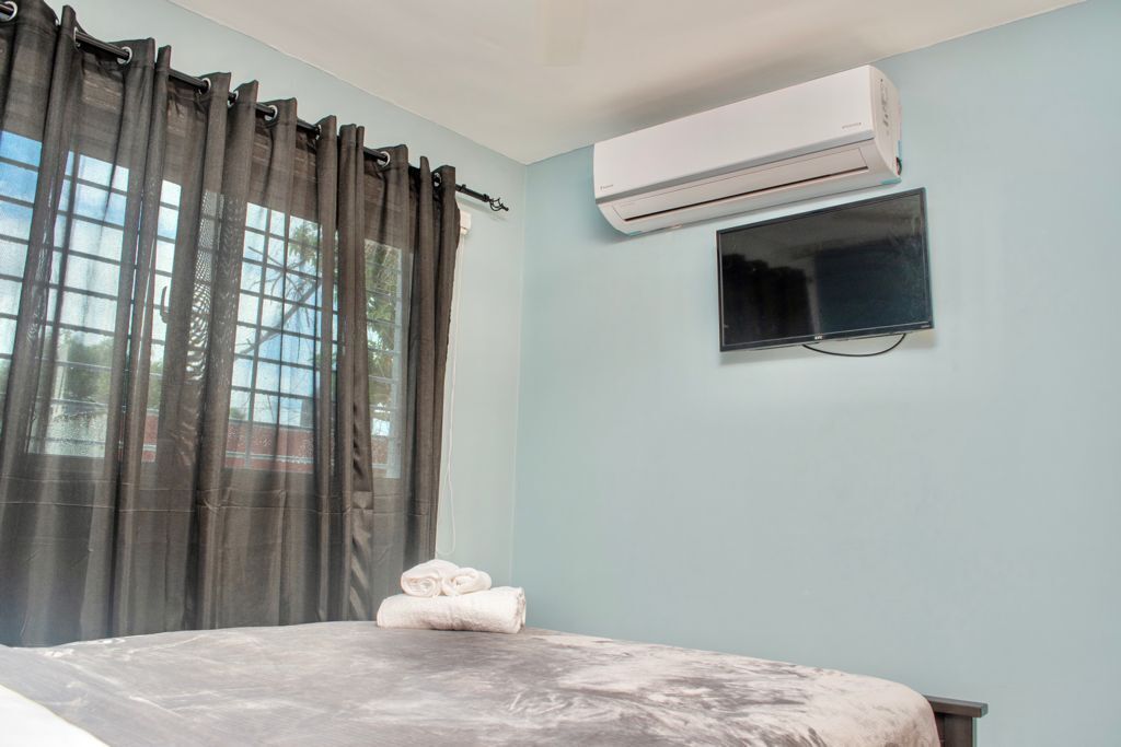 A bedroom with a bed, an air conditioner, a TV, and a window with curtains.