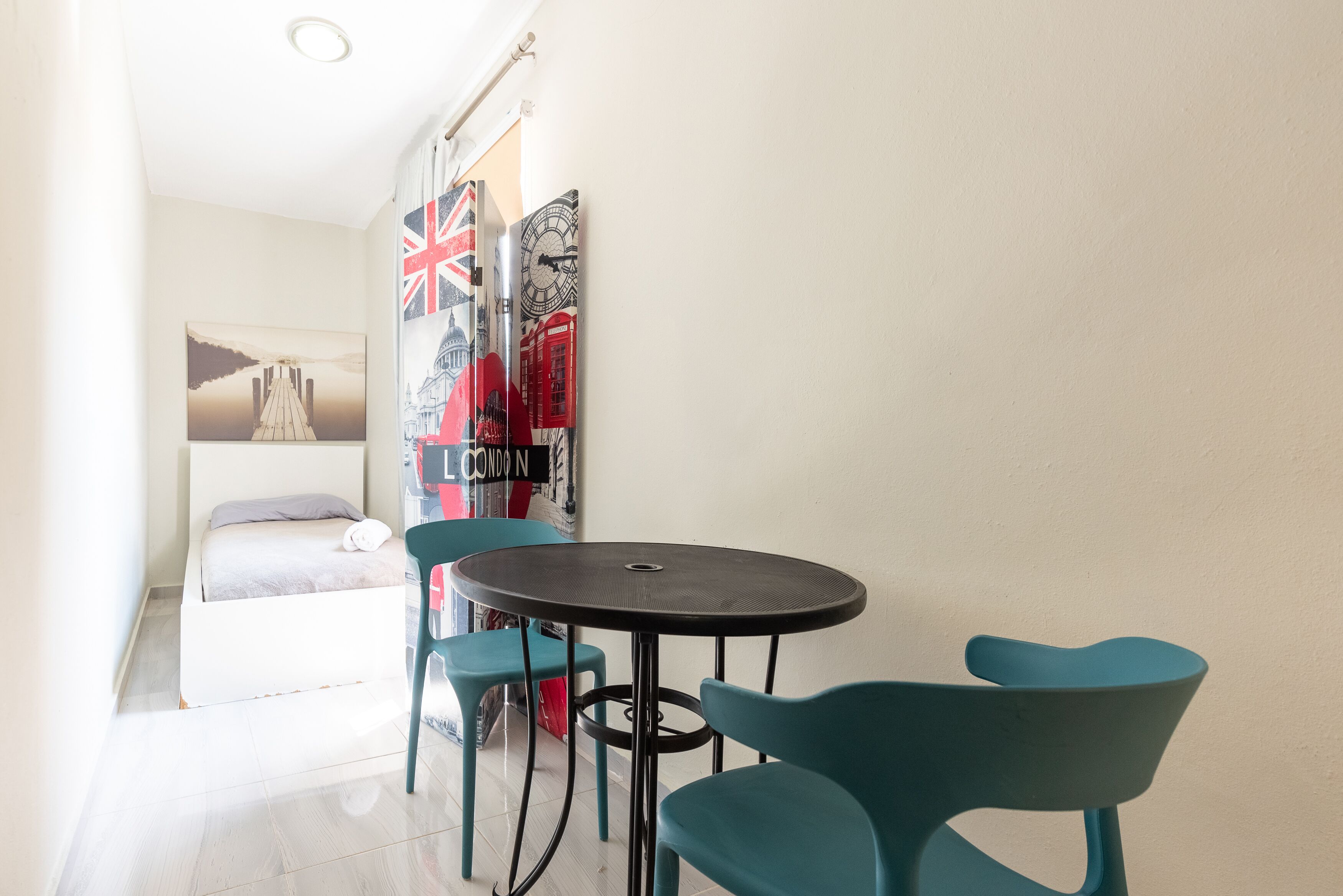 A small room with a bed, a round table, and two chairs. There are wall decorations including a Union Jack and a clock.