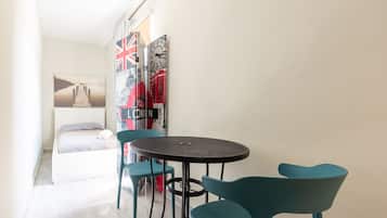 A small room with a bed, a round table, and two chairs. There are wall decorations including a Union Jack and a clock.