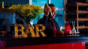 A bar area with illuminated 'BAR' letters, a vase with yellow flowers, and a shelf with bottles. - Hotel Casa Jum (Santiago de los Caballeros)
