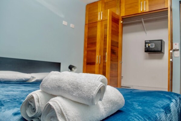 A hotel room with a bed, a wooden wardrobe, and a thermostat on the wall.