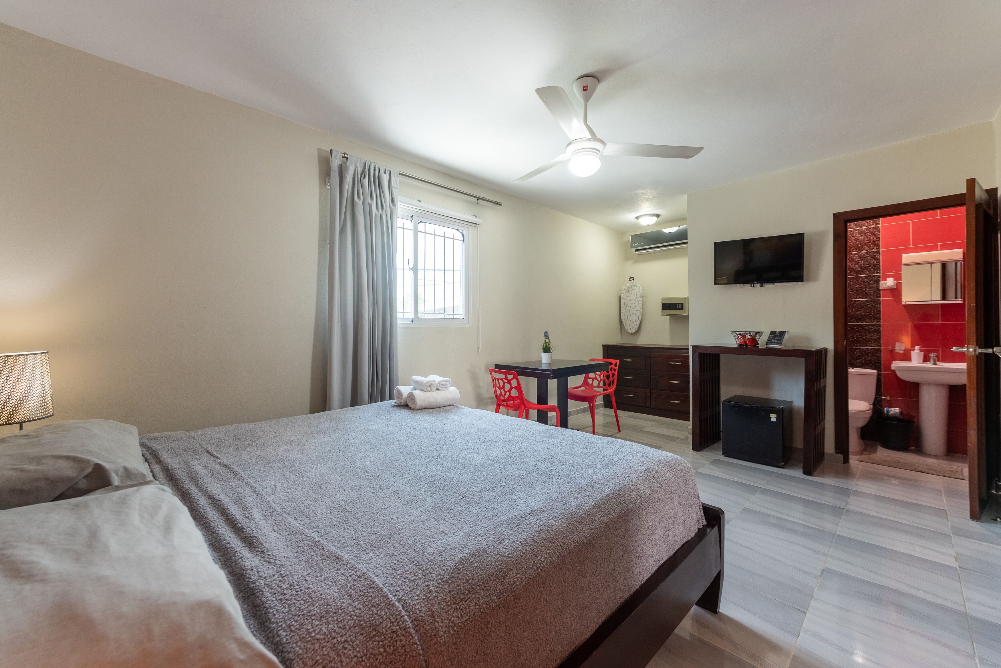 A bedroom with a bed, a desk, a chair, a TV, and a bathroom with a sink and toilet.