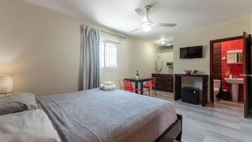 A bedroom with a bed, a desk, a chair, a TV, and a bathroom with a sink and toilet.