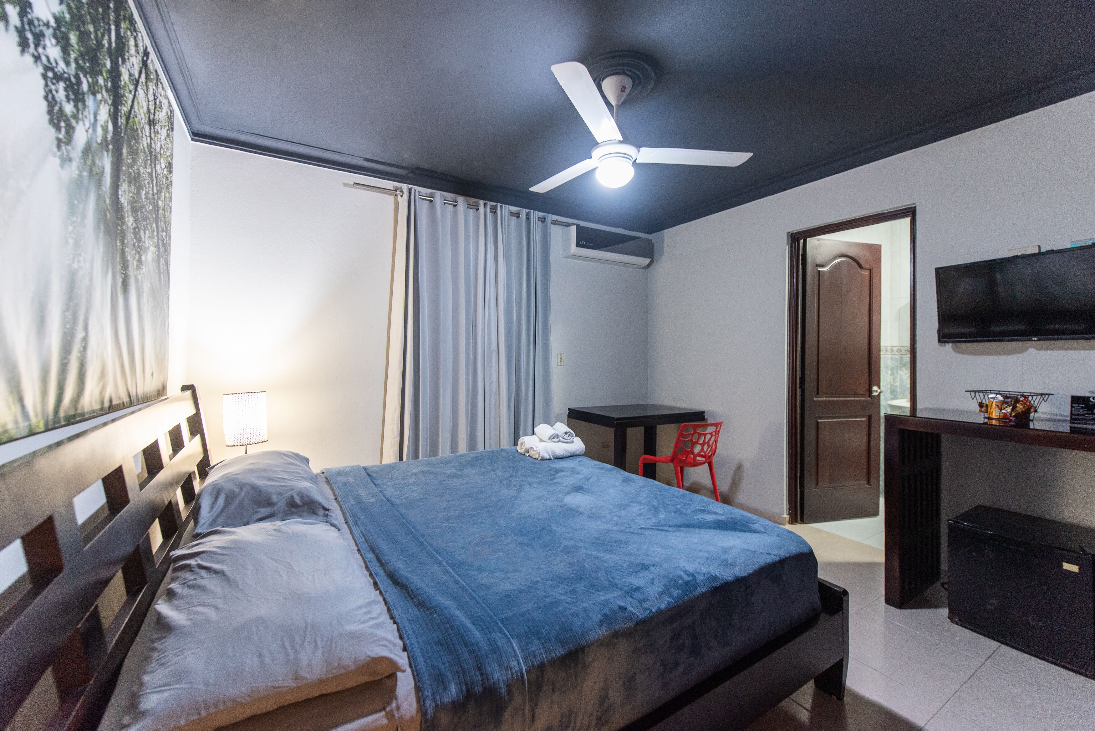 A hotel room with a bed, a desk, a chair, a television, and a ceiling fan.