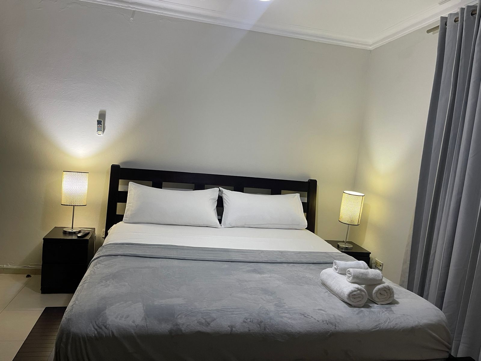 Een net opgemaakt bed met witte lakens, twee bedlampjes en een set handdoeken op het bed.