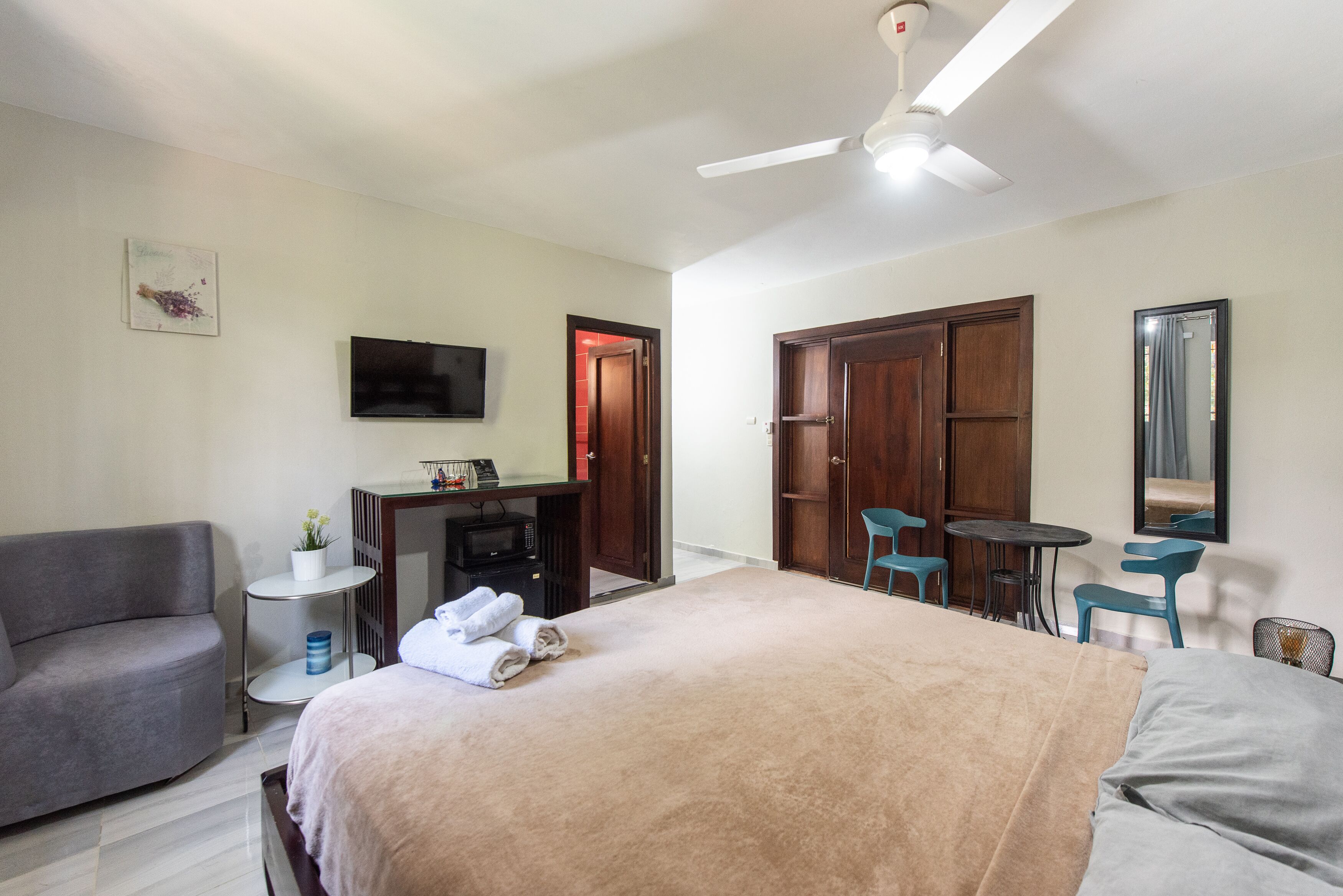 A hotel room with a bed, a sofa, a desk with a computer, a TV, and a ceiling fan.