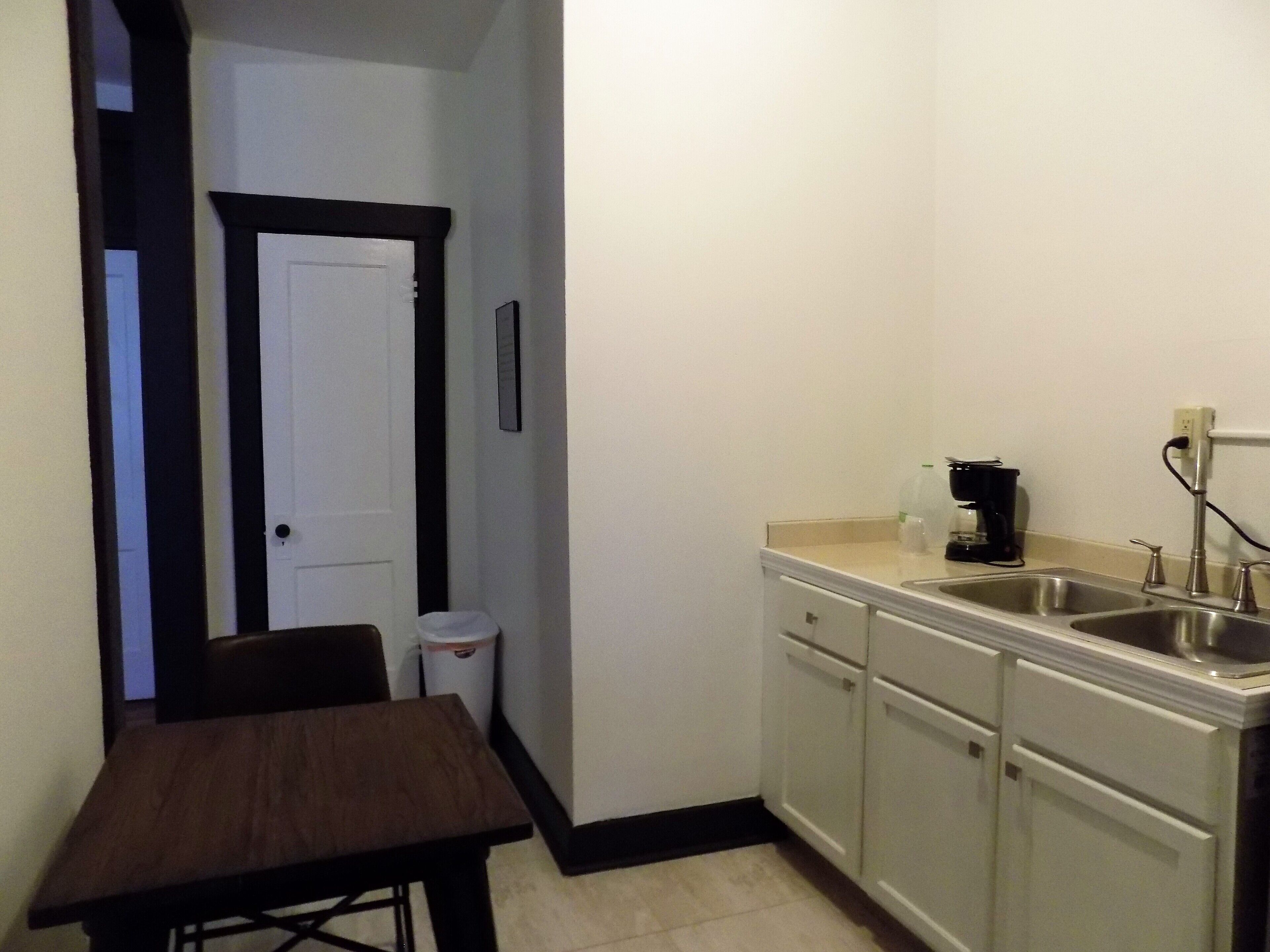 A small kitchen with a sink, a coffee maker, and a trash can.