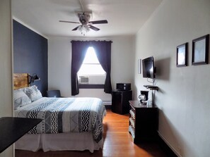 A bedroom with a bed, a ceiling fan, a TV, and a dresser.