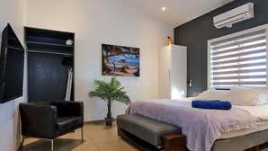 Een moderne slaapkamer met een bed, een bureau, een stoel, een potplant en een schilderij aan de muur.