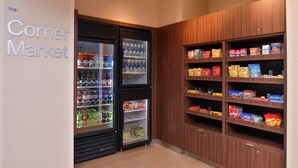 Uma mercearia de esquina com geladeiras para bebidas e prateleiras cheias de lanches e alimentos.