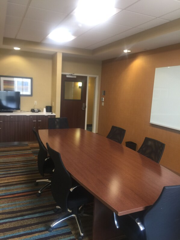 A conference room with a long wooden table, black chairs, a projector screen, and a television on a desk. - Fairfield Inn & Suites by Marriott Farmington (Farmington)