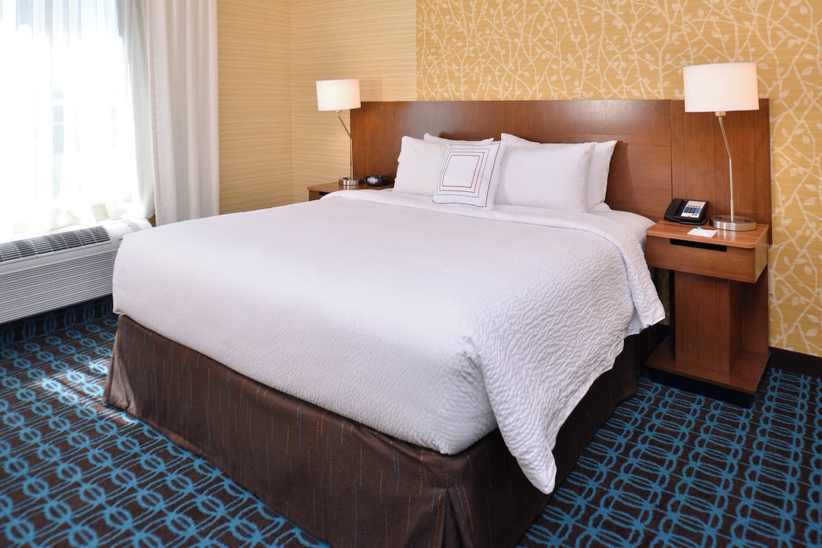 A hotel room with a large bed, two bedside tables with lamps, a patterned carpet, and a window with curtains.