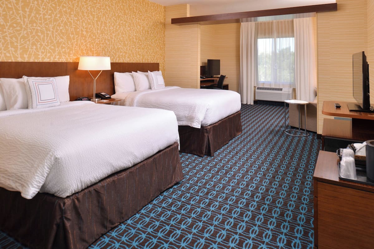 A hotel room with two beds, a desk, a TV, and a window with curtains.