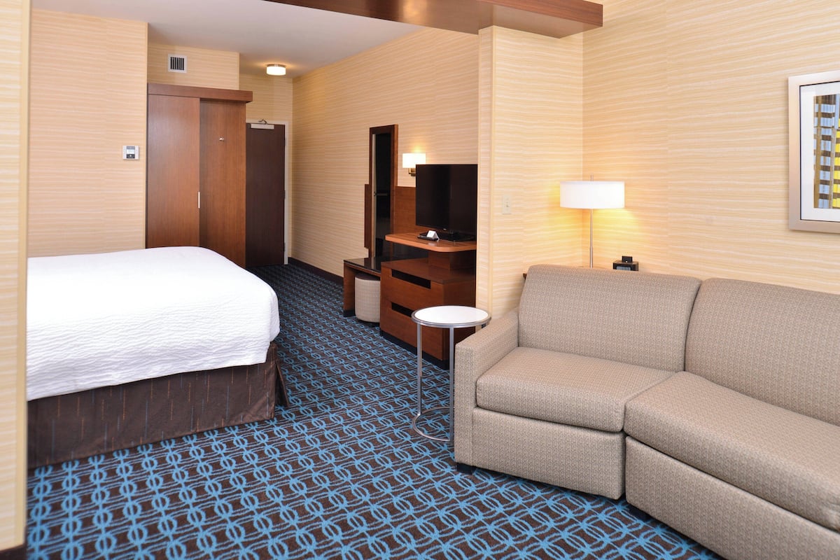 A hotel room with a bed, a sofa, a desk with a lamp, a TV, and a wardrobe.